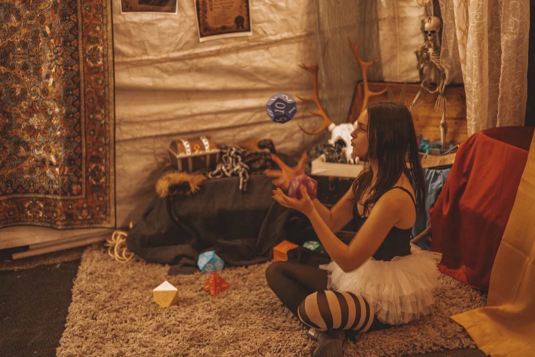 A participant seated in costume tossing oversized polyhedral dice.