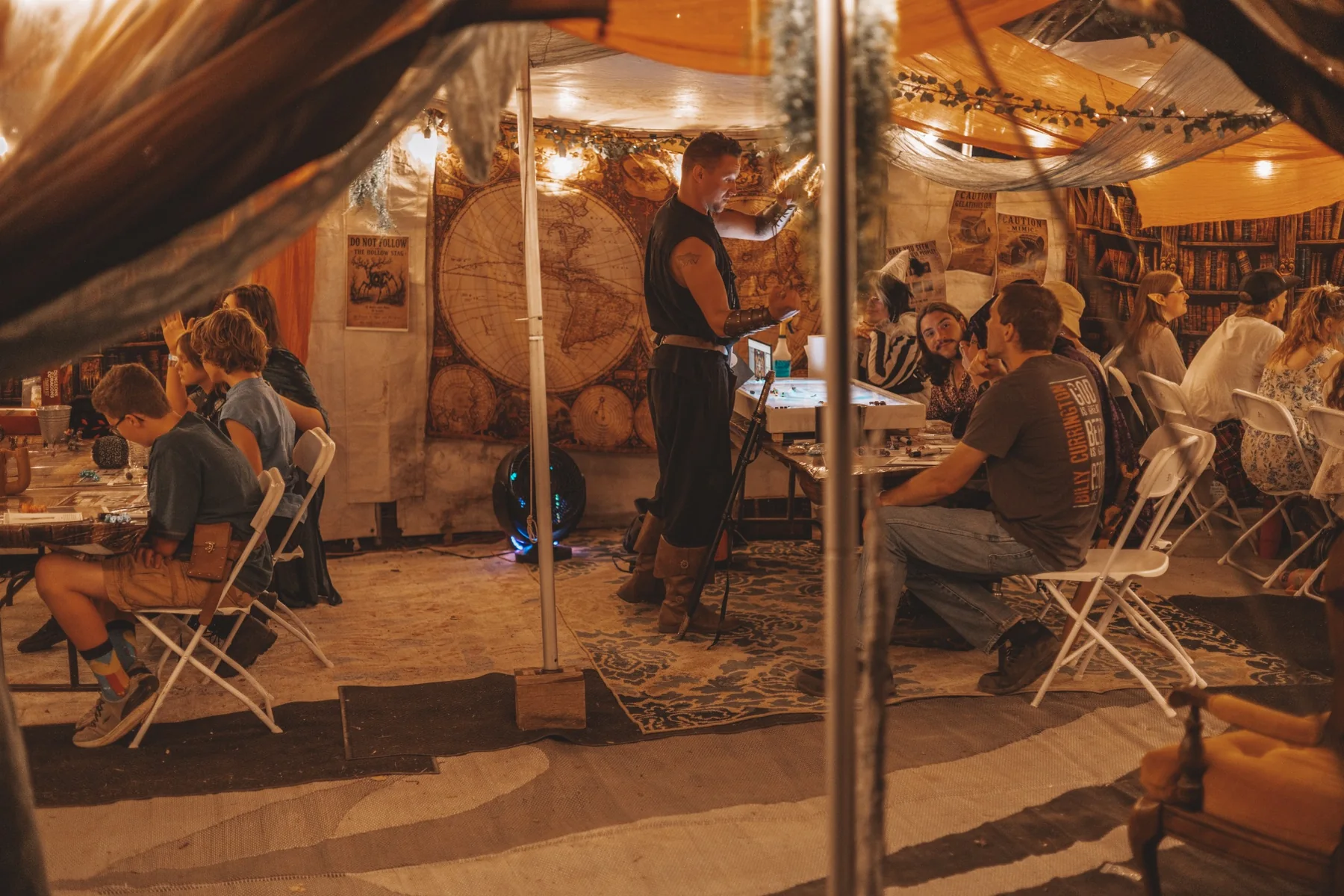 A wide view through the entrance of the Valley of the Nerds Guildhall tent with multiple game tables.