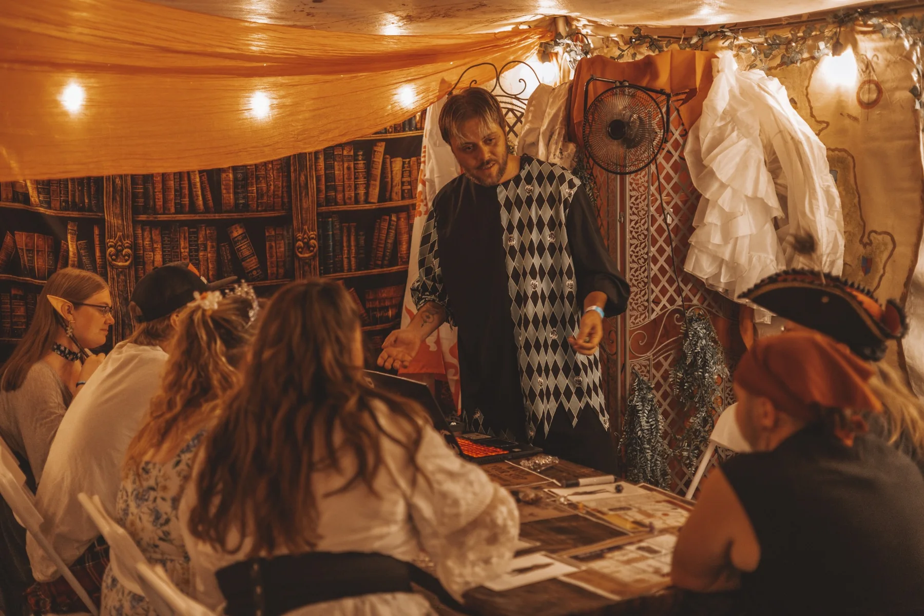 A jester-costumed game master leading players around a tabletop session.