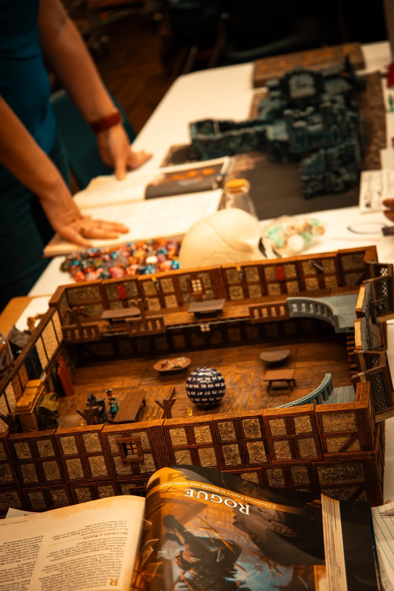 A tabletop scene with miniatures, dice, and a detailed building model.