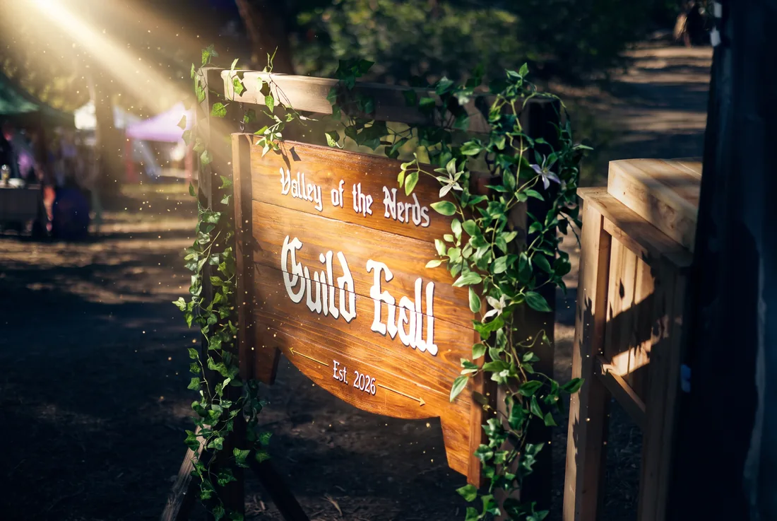 The wooden Valley of the Nerds Guild Hall sign wrapped in ivy and lit by a warm sunbeam.