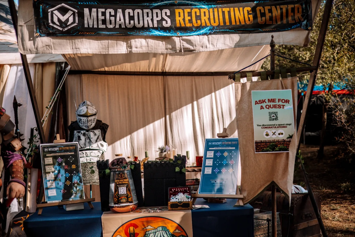 The Valley of the Nerds event welcome table with a recruiting banner, activity schedules, quest sign, and fantasy props